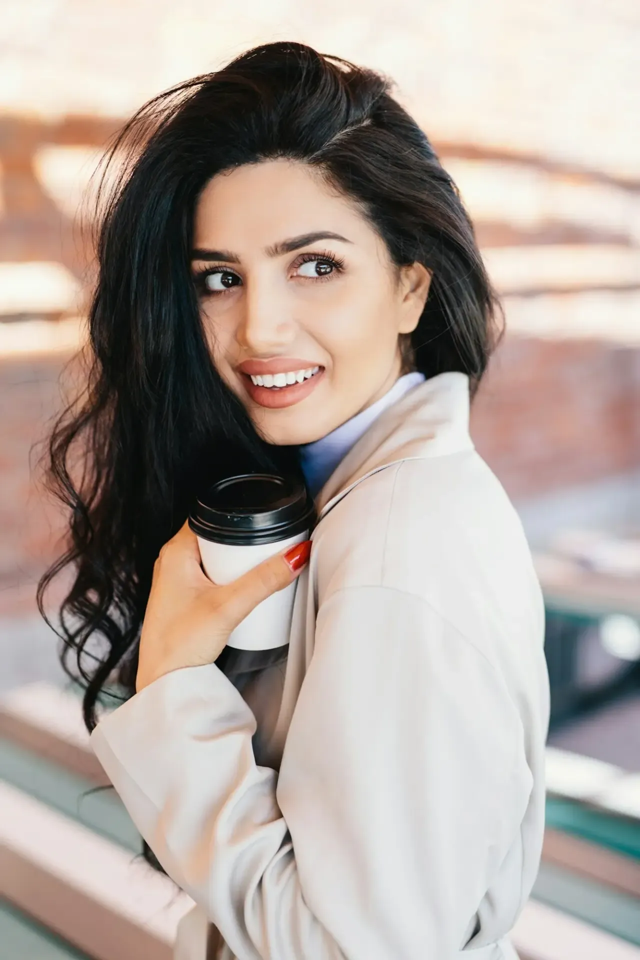 A smiling woman with perfect teeth drinking a cappuccino