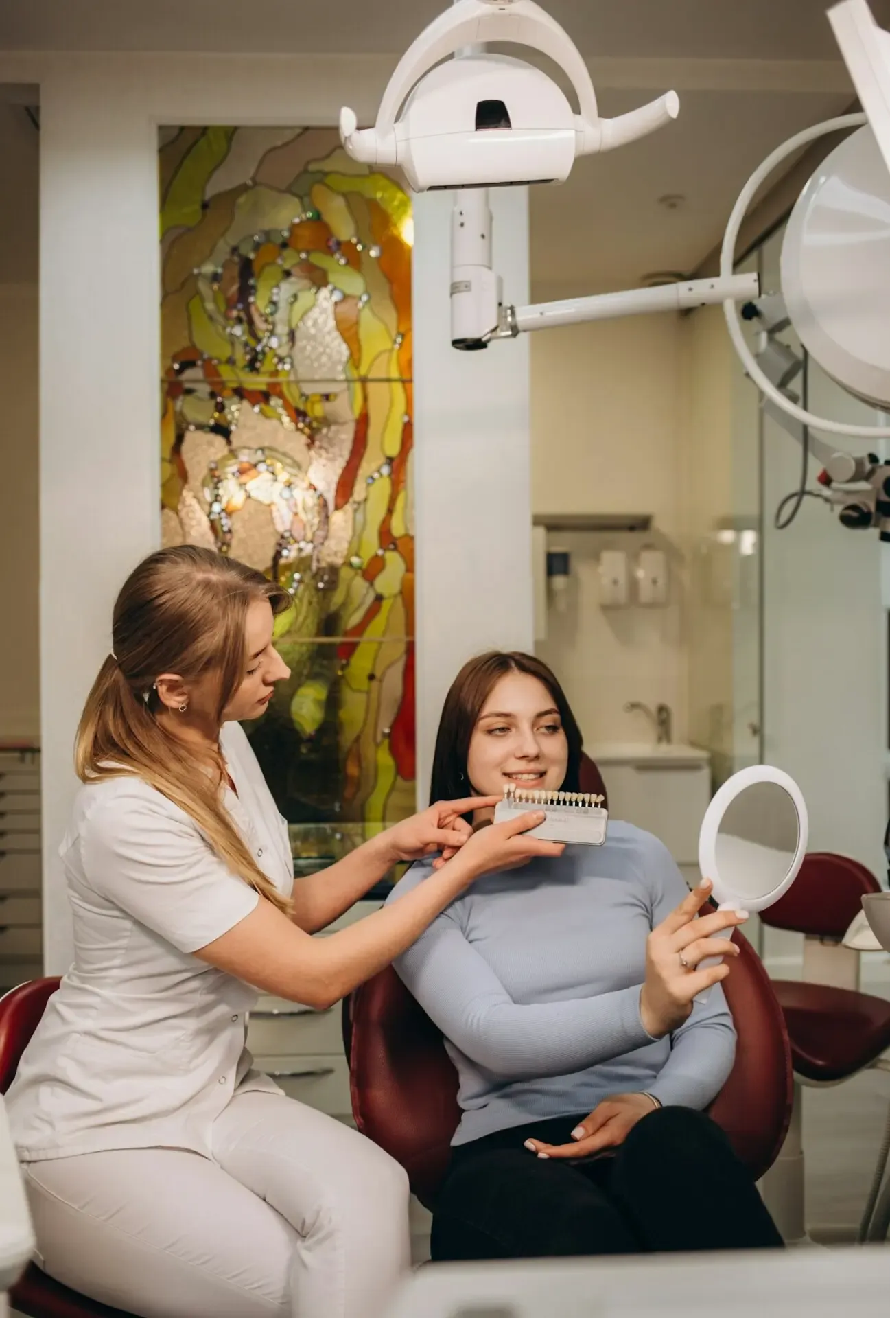 A smiling woman comparing veneer enamel shades with her dentist